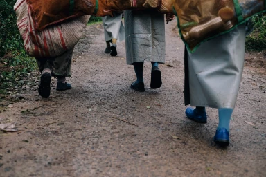 Low angle view of people walking away on a damp dirt path carrying large sacks on their backs for the Ti Origin project.