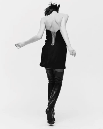 Back view of a woman in a black strapless dress and thigh-high boots against a white background, in a black and white studio shot.