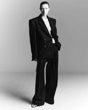 Model wearing an oversized black suit and trousers standing against a seamless grey backdrop.