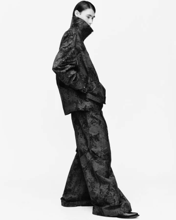 Model wearing a patterned dark jacket and matching trousers against a stark white background.
