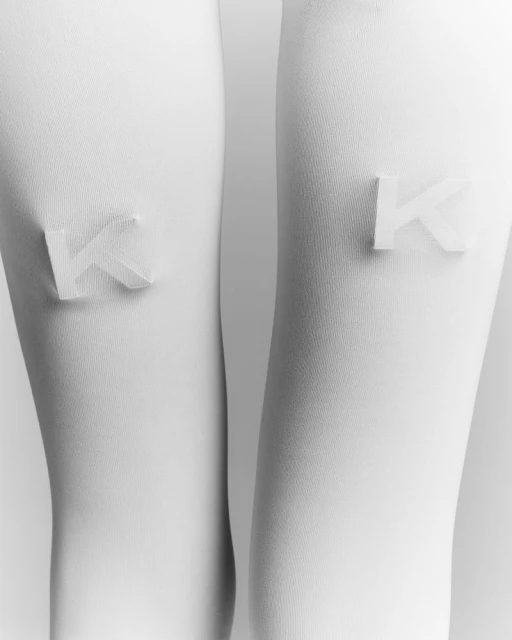 Close-up of a pair of white legs wearing tights, each adorned with a raised, textured 'K' initial, creating a minimalist and modern aesthetic.