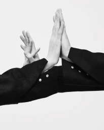 Close-up of hands and arms wearing black garments with silver buttons against a white background.