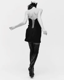 Model seen from behind wearing a strapless black mini dress with lace-up back and high leather boots against a white backdrop