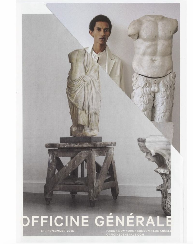 Fashion editorial featuring a man in a suit jacket standing next to classical statues, set against a neutral background.
