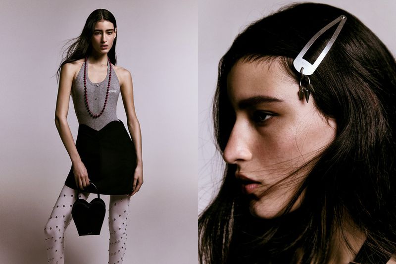 Model in grey halter top and black skirt wearing white tights and holding heart bag against a grey backdrop