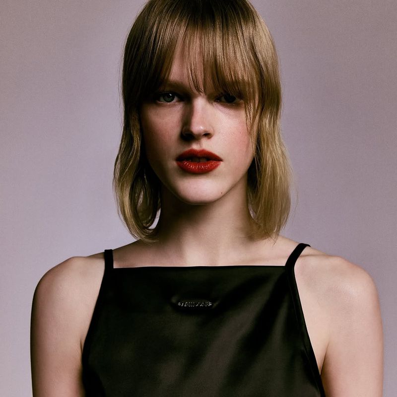 Portrait of a woman with bangs wearing a black top against a plain grey background for WE11DONE