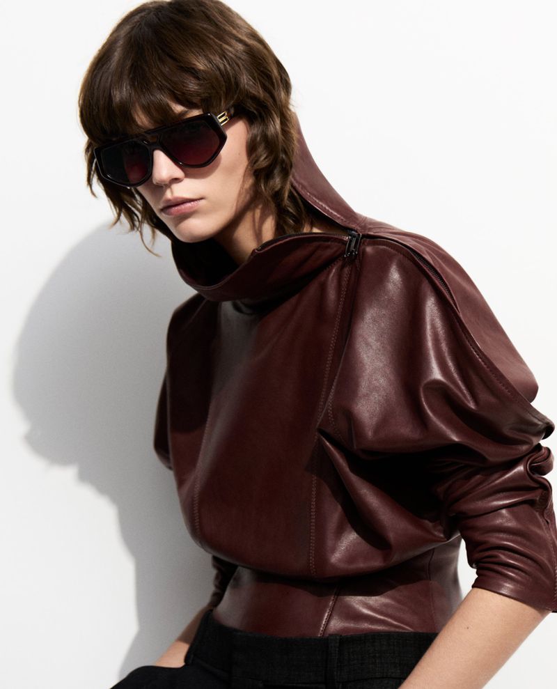 Studio shot of a brunette woman wearing a dark red leather top and sunglasses against a white background, fashion photography.