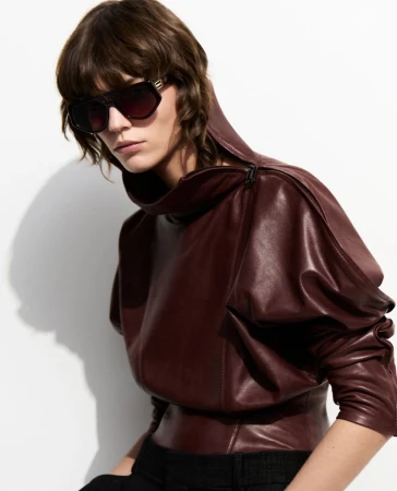 Studio shot of a brunette woman wearing a dark red leather top and sunglasses against a white background, fashion photography.