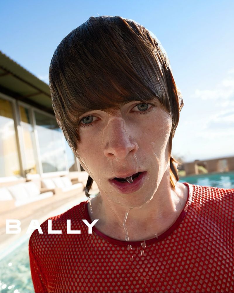 Close-up portrait of a wet-haired adult man wearing a red mesh shirt and with water dripping from his face, posing outdoors.