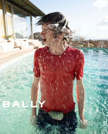 A person in a red shirt is submerged in a turquoise swimming pool, water splashing all around them, with a blurred house in the background.
