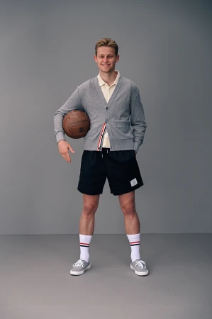 Full-shot of a smiling man in sportswear holding a soccer ball, set against a grey background in a studio setting. Fashion, sport.