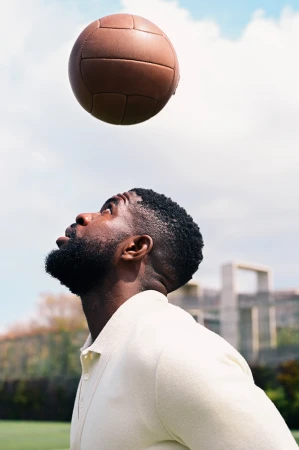 Black man looking up at a vintage leather football in an outdoor setting for Thom Browne and Fc Barcelona