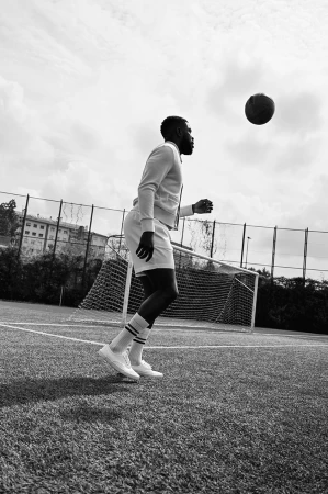A Black male athlete in sportswear heading a soccer ball on a green field, overcast sky backdrop, promoting sports, fitness, and healthy lifestyle.