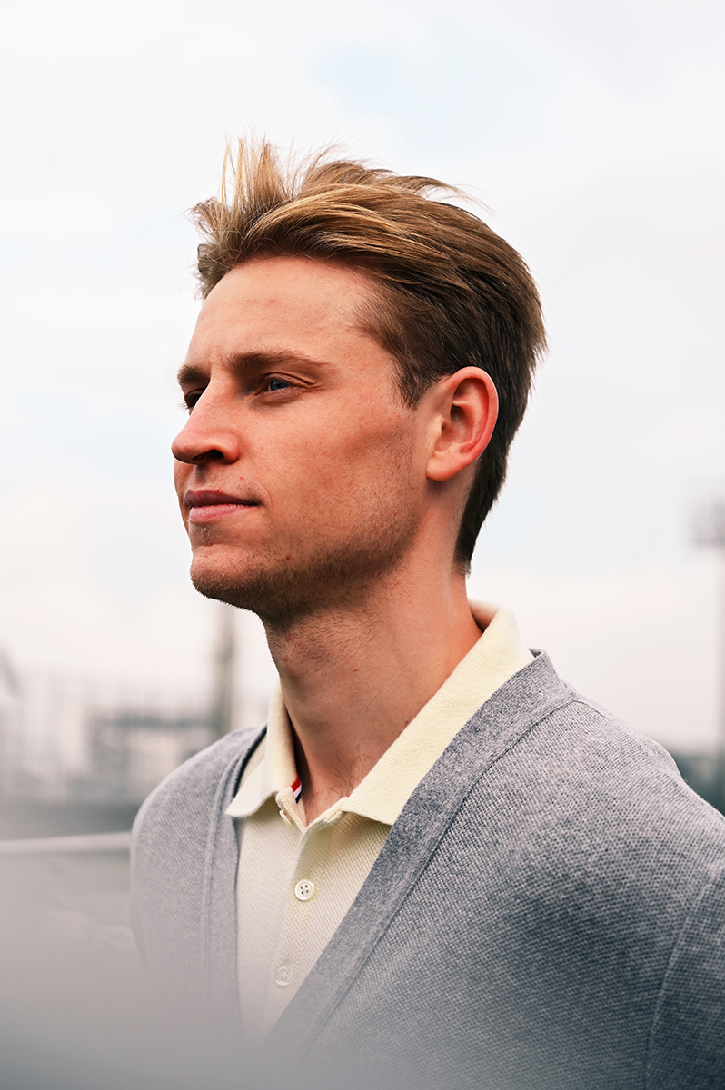 Blond man in gray cardigan and polo shirt against a cloudy sky. Portrait of a handsome male model looking off into the distance.