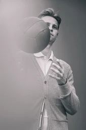 Man wearing a cardigan holding a football in front of a grey seamless background
