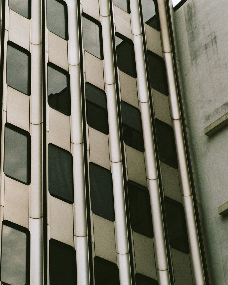 Exterior architecture of a modern office building with diamond-shaped windows and metallic facade, captured on a cloudy day in an urban setting.