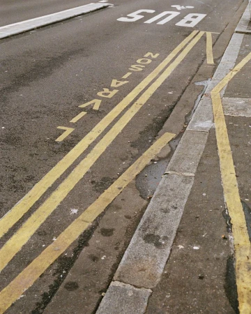 Street view of asphalt road with double yellow lines marking a bus lane, and gray concrete curb visible on the right edge of the frame.