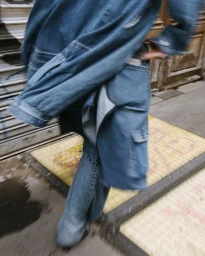 Motion blurred close-up shot of a person wearing a blue denim jacket and matching jeans walking down a city street.