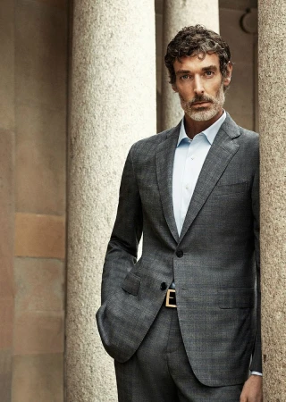 Portrait of a man in a gray suit standing between stone columns, looking at the camera with a neutral expression.