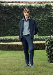Model standing on a lush green lawn wearing a navy blue zip jacket over a light blue polo shirt and matching trousers.