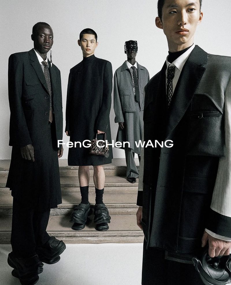 Group of four fashion models wearing dark, structured clothing and unique shoes, posing on stairs in a studio setting.