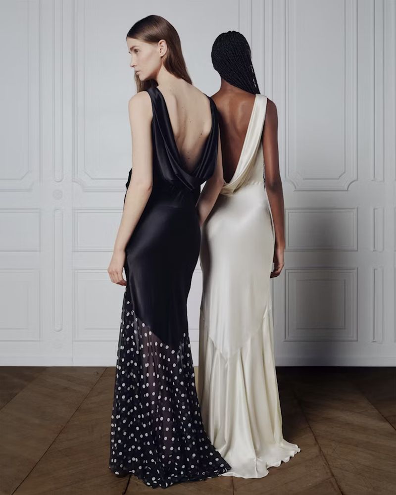 Two women stand side-by-side in floor-length gowns. One wears a black silk dress with polka dot mesh, the other an off-white silk gown.