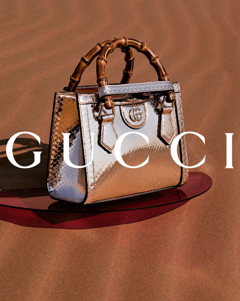Gucci handbag with bamboo handle is displayed on a red base against a neutral backdrop. The bag has a metallic sheen and snakeskin texture.
