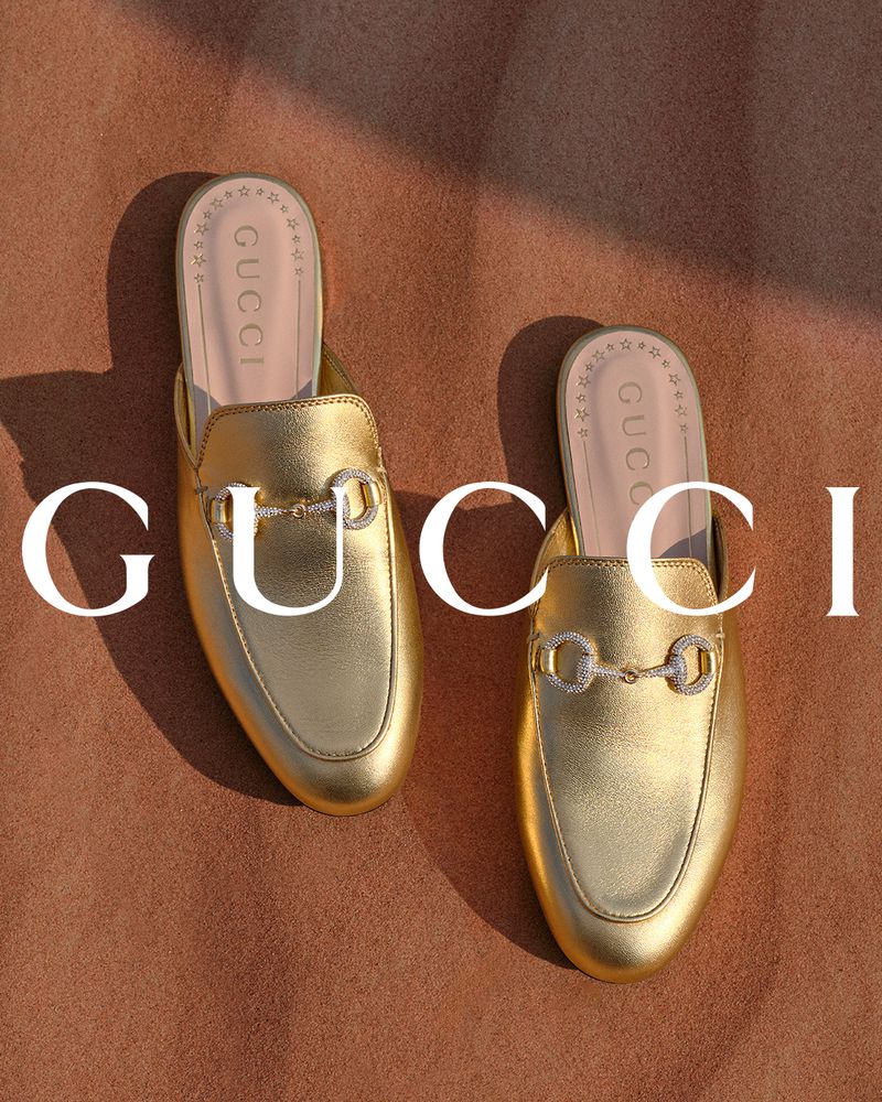 Elevated view of two golden Gucci mules on a tan background featuring the brand logo, stylish footwear, and fashion product photography.