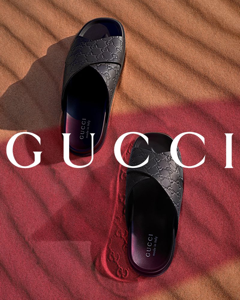 Gucci slide sandals on a tan and red background. Two stacked Gucci sandals, top and bottom, with logo printed on the background.