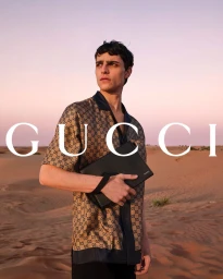 Male model wearing a monogram silk short-sleeve shirt in a desert setting during sunset for Gucci