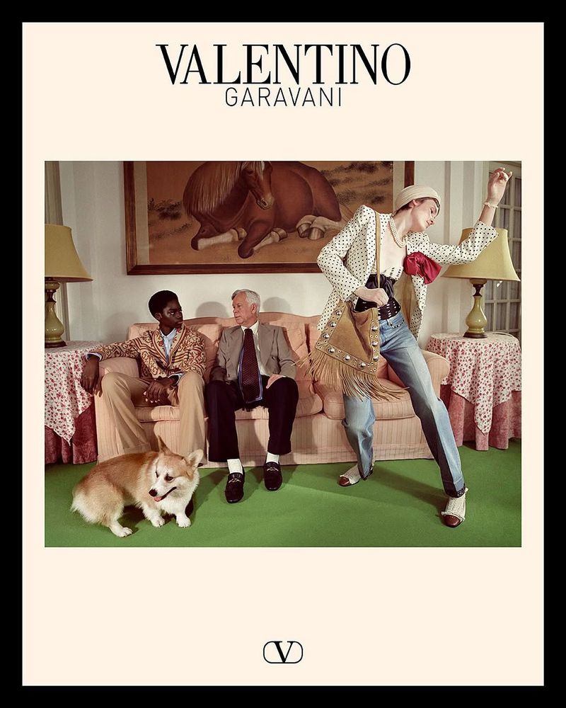 Valentino Garavani fashion ad featuring three adults and a corgi dog in an indoor setting with a painting and vintage furniture.