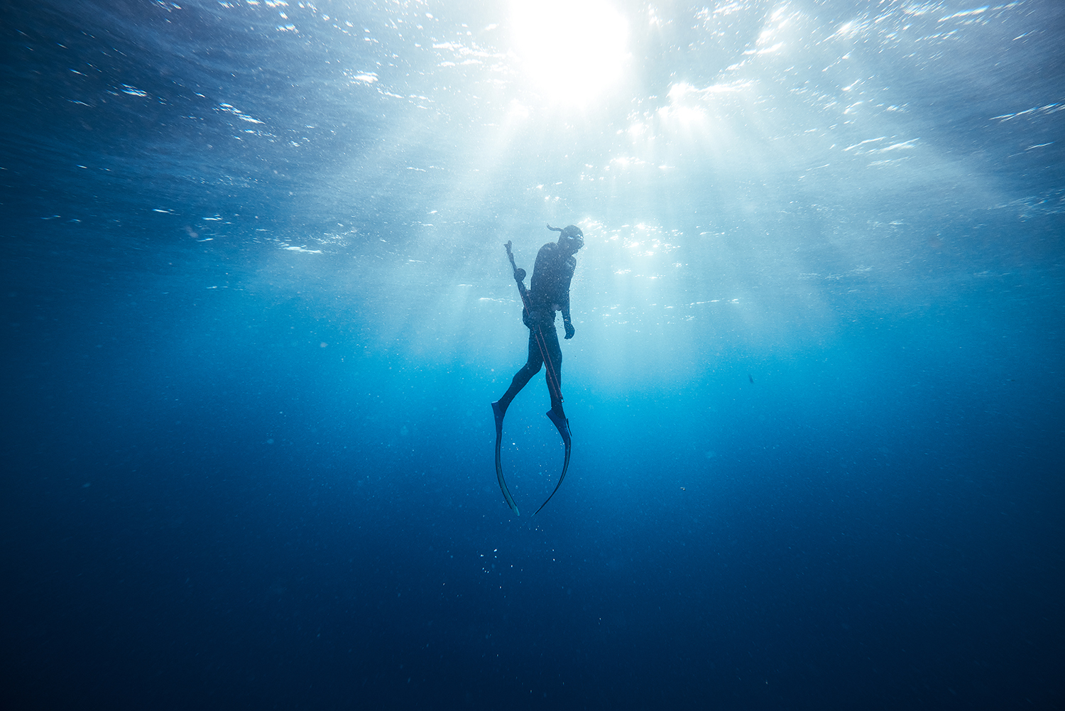 Underwater photo of a free diver swimming in clear blue ocean water with sunlight shining from above creating a serene and peaceful scene.