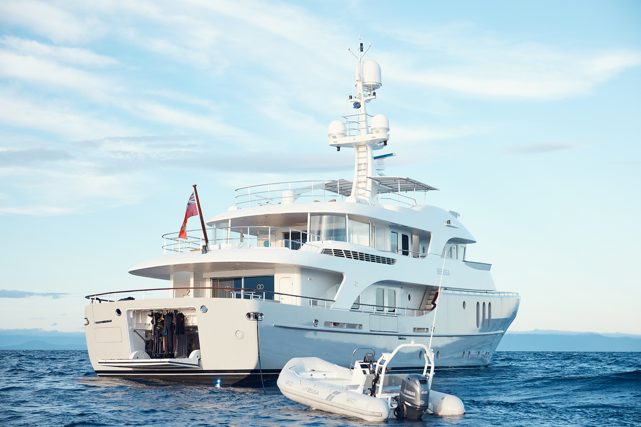 A large, luxury yacht is anchored in the ocean next to a small motorized raft under a bright sky, showcasing maritime leisure.