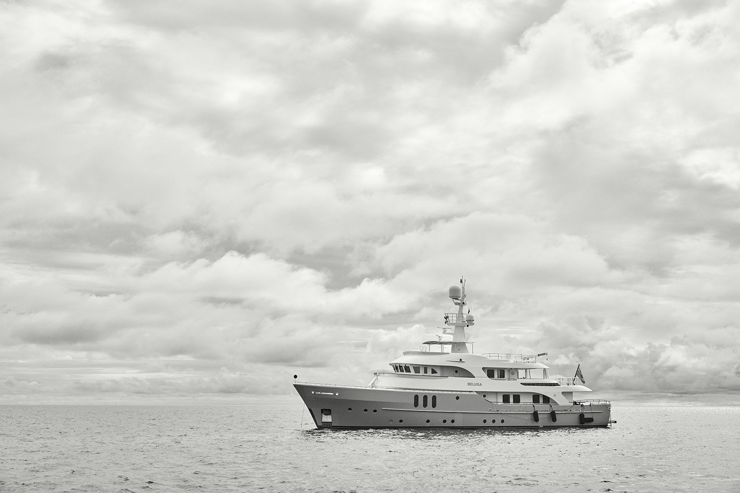 Luxury yacht 'BELUGA' sails calm ocean water under cloudy sky. Monochrome shot with prominent water, sky and ship details. Seascape.