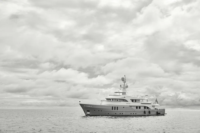 Luxury yacht 'BELUGA' sails calm ocean water under cloudy sky. Monochrome shot with prominent water, sky and ship details. Seascape.