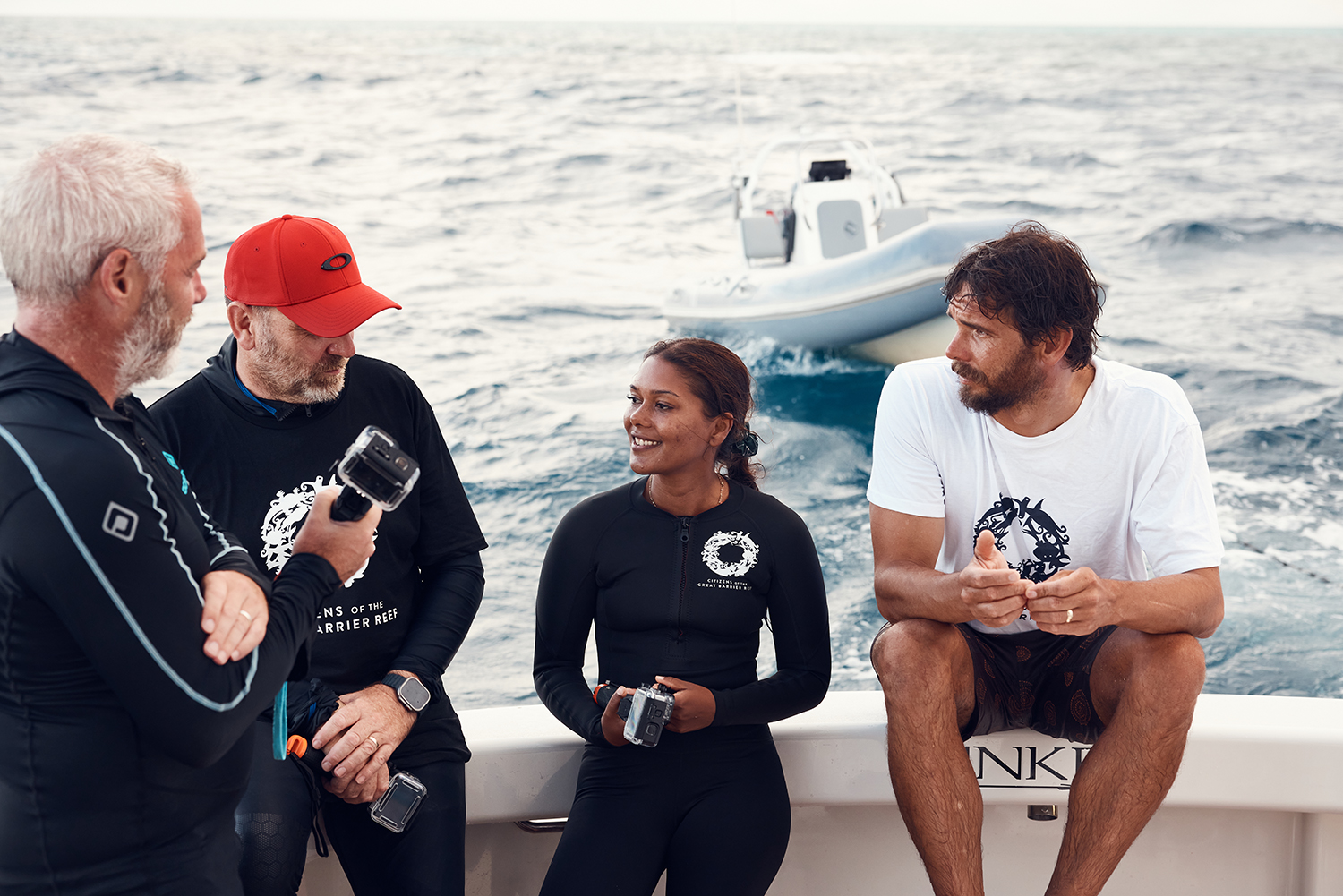 Four people stand on a boat discussing ocean conservation with an inflatable boat in the background on open water during the daytime.