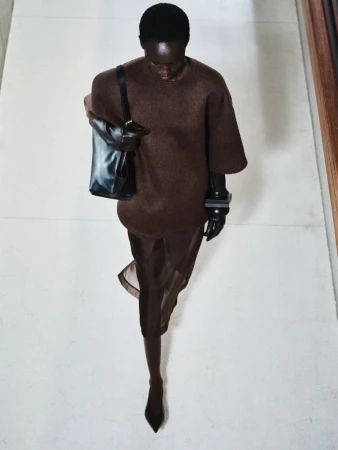 Runway fashion: a Black model presents a brown dress with a black tote bag in a minimalist interior setting, captured from a high-angle perspective.
