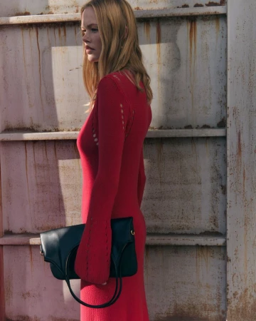 Model in a red knit dress holding a dark handbag against a rusted industrial structure for SEMICOUTURE SS25