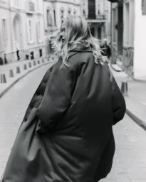 Model Emma Stern Nielsen walking on an urban street wearing a long dark coat for SEMICOUTURE SS25