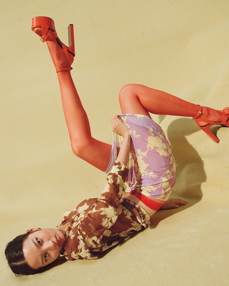 Model lying on back with legs raised wearing red platform sandals and floral skirt for Versace S/S 25