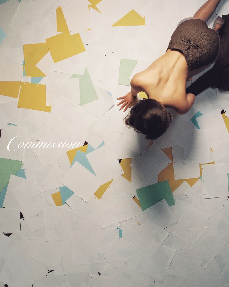 Overhead shot of a woman with her hand on the floor covered with paper cut-outs in yellow, white, light green, and light blue.