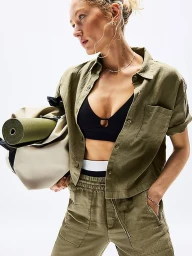 Model in olive green shirt holding duffel bag with yoga mat against white background