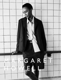 Black and white portrait of a female model wearing a dark blazer and shirt against white tiled wall