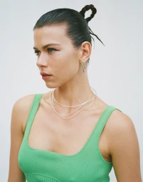 Georgia Fowler wearing a green ribbed tank top, layered silver necklaces, and sculptural earrings against a plain background