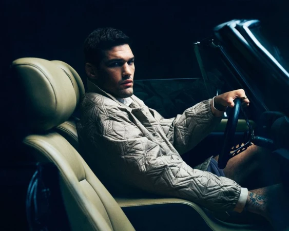 Man driving a convertible in a low-lit setting, wearing a patterned jacket, showcasing modern automotive lifestyle and fashion.