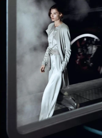 Fashionable adult woman strides confidently in light-blue pantsuit, cinched with an elaborate belt, against a backdrop of billowing smoke.
