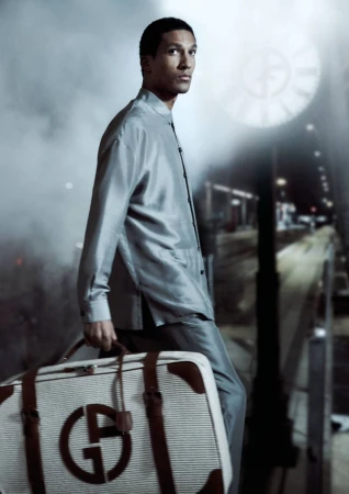 Man in suit at train station with Armani luggage. Male fashion model poses with designer bag at an outdoor railway platform.