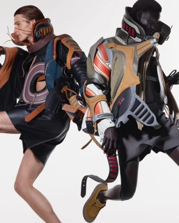 Two adult fashion models strike dynamic poses in futuristic, deconstructed outfits against a bright white backdrop in a studio shot.
