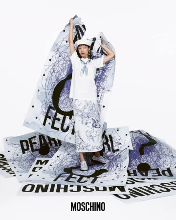 Fashion shot of a woman in a sailor hat and clothing, surrounded by oversized posters with graffiti-style text and black scribbles.