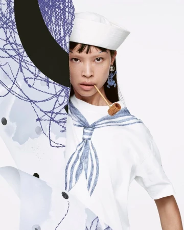 Close-up studio shot of an Asian adult female in a sailor hat and T-shirt, holding a small pipe, with blue and white abstract designs.